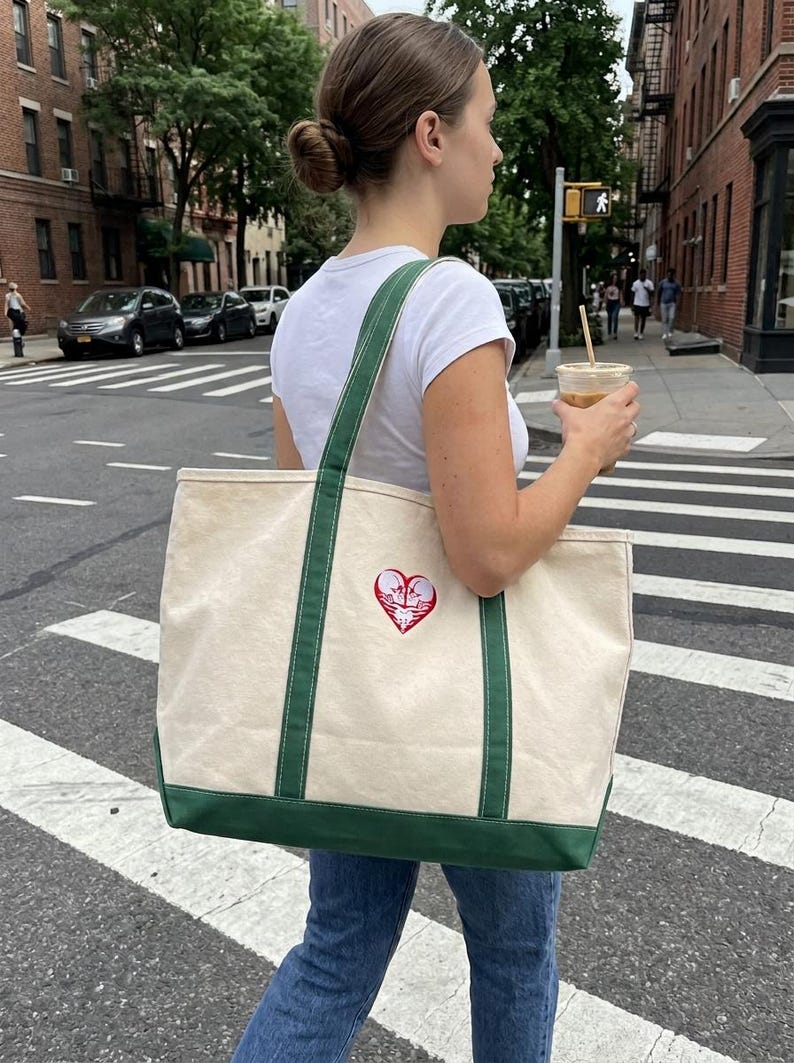 Canvas tote bag featuring a red and white skeleton couple heart embroidery, carried as part of a casual city outfit.