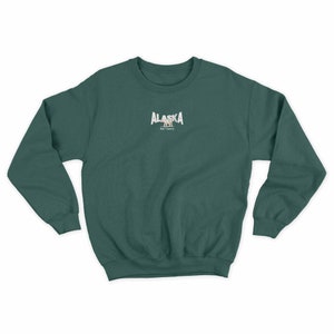 May include: A dark green sweatshirt with a white graphic of the word "ALASKA" with a bear silhouette underneath. The text "Bear Country" is below the bear.
