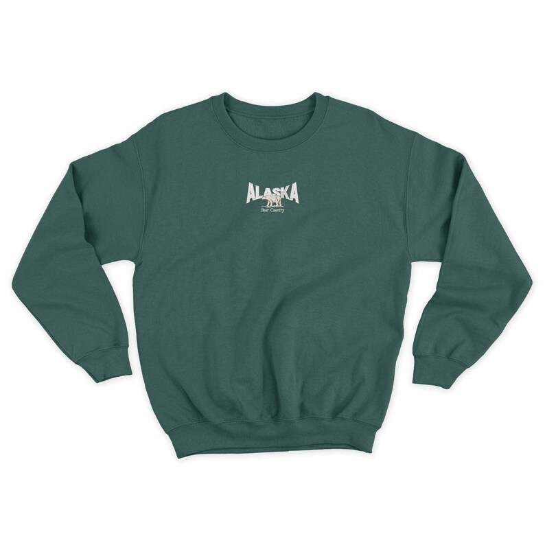 May include: A dark green sweatshirt with a white graphic of the word "ALASKA" with a bear silhouette underneath. The text "Bear Country" is below the bear.