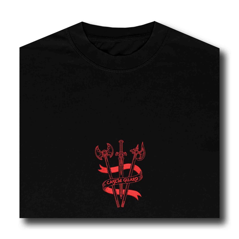 K&ouml;nnte beinhalten: Schwarzes T-Shirt mit einem roten gestickten Design aus drei Waffen, zwei &Auml;xten und einem Schwert, die &uuml;ber einem roten Band mit dem Text "CASTLE GUARD" gekreuzt sind.