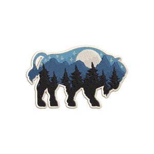 Op de afbeelding: Een geborduurde patch met een silhouet van een bizon met een berg- en maanscène erin. De scène is in blauw en wit met een volle maan en sterren.