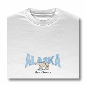 May include: White t-shirt with a blue and white graphic of the word "Alaska" with a polar bear walking below the text. The text "Bear Country" is below the bear.