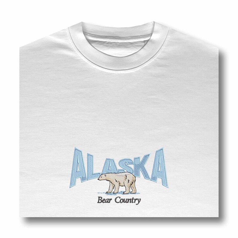 May include: White t-shirt with a blue and white graphic of the word "Alaska" with a polar bear walking below the text. The text "Bear Country" is below the bear.