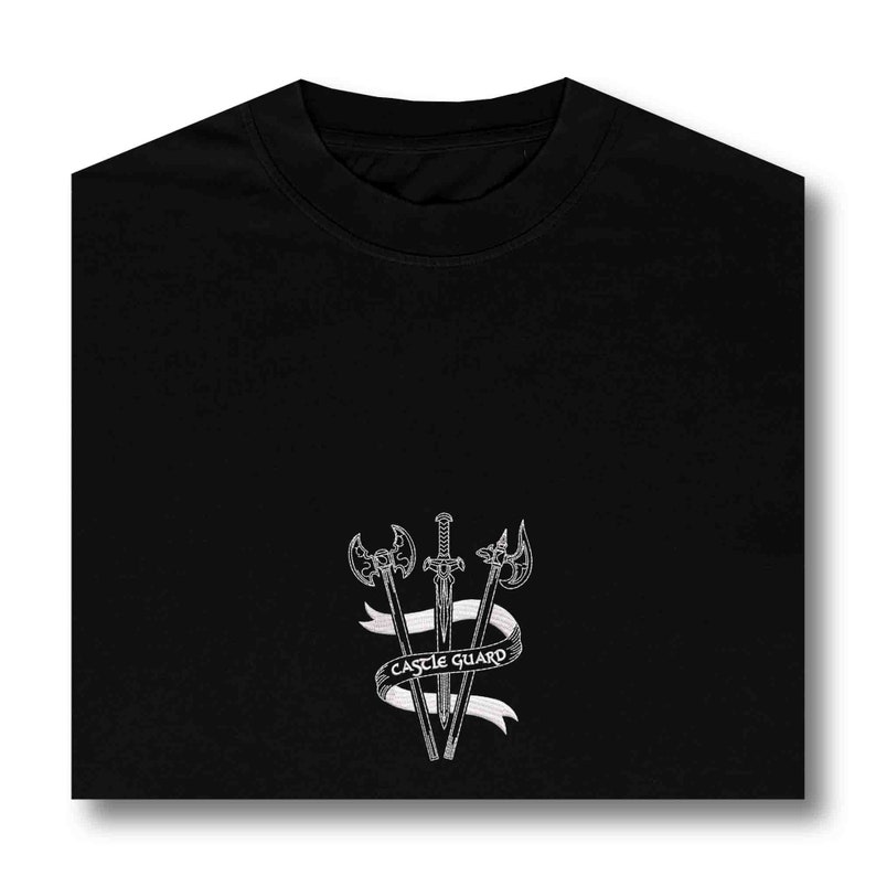 K&ouml;nnte beinhalten: Schwarzes T-Shirt mit einer wei&szlig;en Grafik von drei Schwertern und einer Axt mit einem Banner, auf dem "CASTLE GUARD" steht.
