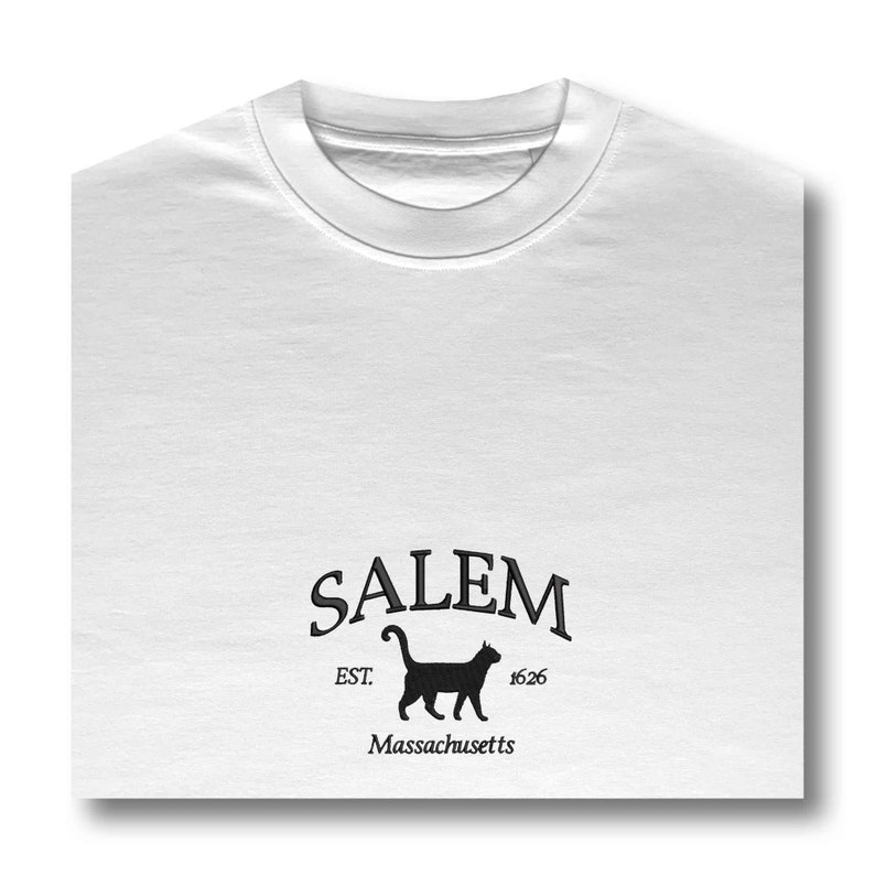 K&ouml;nnte beinhalten: Wei&szlig;es T-Shirt mit einem schwarzen grafischen Design, auf dem "SALEM EST. 1626 Massachusetts" mit einer schwarzen Silhouette einer Katze steht.