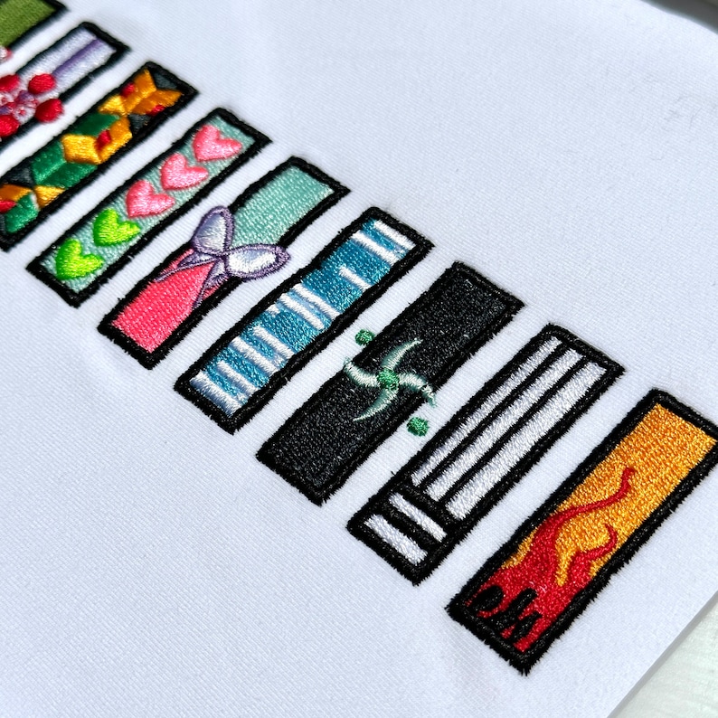 以下が含まれることがあります： ハート、蝶、ストライプ、渦巻き、炎など、さまざまなデザインの刺繍パッチが並んでいます。パッチはすべて黒で縁取られており、白い背景に配置されています。