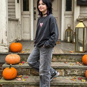 Dark oversized sweatshirt featuring a small red and white skeleton love heart embroidery on the chest, styled in a gothic autumn outfit.