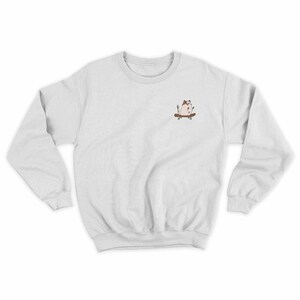 Op de afbeelding: Een wit sweatshirt met een klein geborduurd beeld van een skateboardende kat op de linker borst.