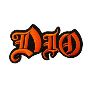 May include: Embroidered patch featuring the word "DIO" in stylized orange lettering on a black background. The patch has a decorative, gothic-style font and is likely designed for application on clothing or accessories.