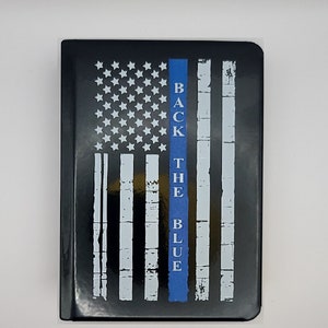 May include: Black and white American flag with a blue stripe down the center. The text "Back the Blue" is printed on the blue stripe.