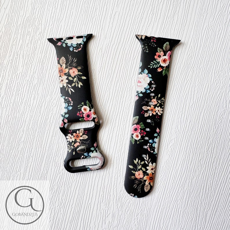 May include: Black silicone Apple Watch band with a floral print featuring pink, orange, and blue flowers. The band has a black buckle and is compatible with Apple Watch Series 4 and later.