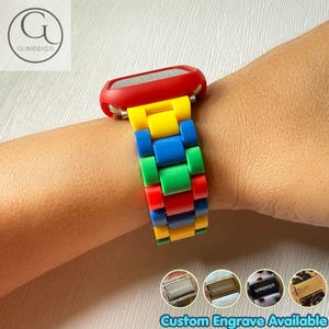 Puede incluir: Una correa de reloj inteligente con una carcasa protectora roja y una correa de eslabones multicolor en amarillo, azul, verde y rojo. La correa consta de segmentos rectangulares. Cuatro imágenes circulares muestran cierres metálicos con el texto GOBANDZUS.