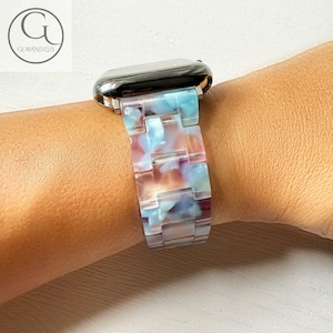Peut inclure: Un bracelet de montre avec un design marbré coloré dans les tons de bleu, rose et blanc. Le bracelet est attaché à un cadran de montre argenté. Le bracelet est composé de maillons rectangulaires.