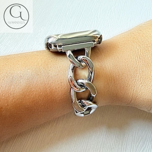 May include: A silver-colored watch band with a chain link design. The band is attached to a watch face and is worn on a wrist. The band is made of a shiny metal and has a polished finish. The watch band is a stylish accessory.