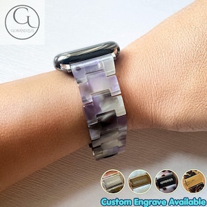 Pode incluir: Uma pulseira de relógio com padrão marmorizado em tons de roxo, branco e cinza com elos retangulares interligados. A pulseira está presa a uma caixa de relógio de metal escuro. Quatro ícones circulares mostram diferentes opções de fechos.