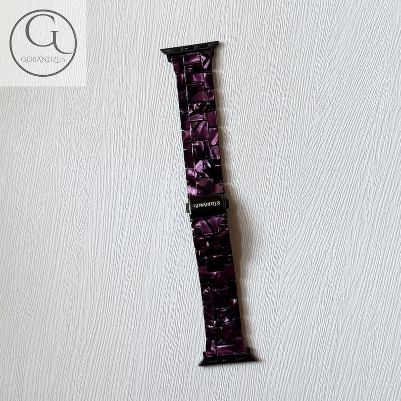 May include: A dark purple watch band featuring a glossy, marbled resin link design with black metal connectors at both ends. The central clasp is black and displays the white text GOBANDZUS, matching the logo visible in the top left corner.