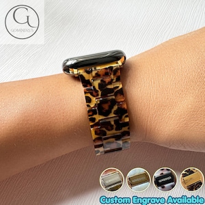 Puede incluir: Una correa de reloj con un patrón de leopardo marrón y negro con acabado brillante. La correa consta de eslabones rectangulares y está unida a una esfera negra. Cuatro iconos circulares pequeños en la parte inferior muestran opciones de grabado.
