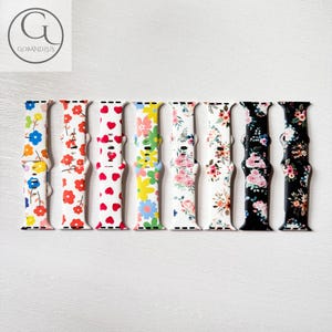 Op de afbeelding: Acht verschillende Apple Watch bandjes met bloemenpatronen. De bandjes zijn gemaakt van siliconen en zijn verkrijgbaar in verschillende kleuren, waaronder wit, zwart, roze en blauw.