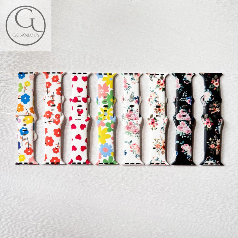 May include: Eight different Apple Watch bands with floral patterns. The bands are made of silicone and come in a variety of colors, including white, black, pink, and blue.