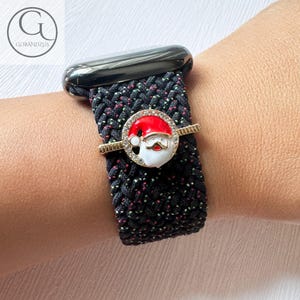 Puede incluir: Pulsera de reloj trenzada negra y verde con un dije de Papá Noel dorado. El dije tiene un gorro rojo, barba blanca y un borde dorado.
