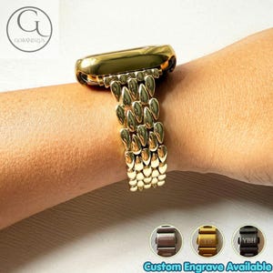 Könnte beinhalten: Ein goldfarbenes Metall-Uhrenarmband mit einem mehrgliedrigen Design aus abgerundeten, tropfenförmigen Segmenten. Das Armband ist an einem Uhrengehäuse befestigt. Drei kleine kreisförmige Einsätze unten zeigen braune, goldene und schwarze Metalloptionen.