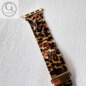 Puede incluir: Banda de reloj Apple dorada con estampado de leopardo. La banda est&aacute; hecha de un material pl&aacute;stico duro y tiene un cierre de metal dorado.