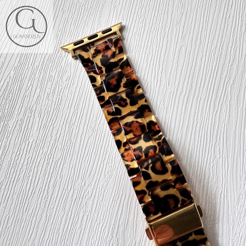 Puede incluir: Banda de reloj Apple dorada con estampado de leopardo. La banda est&aacute; hecha de un material pl&aacute;stico duro y tiene un cierre de metal dorado.