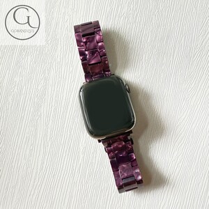 May include: A smartwatch with a dark screen and a link-style watch band made of purple marbled resin. The band features rectangular interlocking pieces with a glossy finish. The logo GOBANDZUS is visible in the upper left corner of the image.