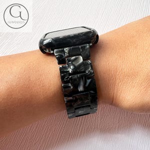 May include: Black and white marbled watch band with a black case. The band is made of a hard plastic material and has a sleek, modern design.