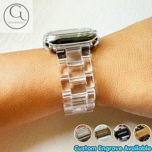 May include: A clear, transparent watch band with a link-style design, featuring a metallic clasp. The band is shown attached to a watch face. Four small circular icons at the bottom display various clasp colors and the text Custom Engrave Available.