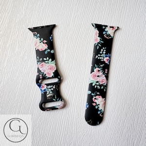May include: A black watch band with a floral print featuring pink, blue, and white flowers on a black background. The band is made of silicone and has a buckle closure.