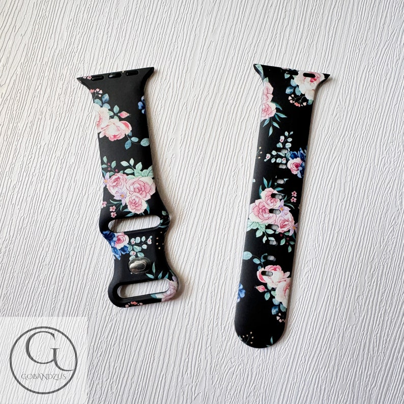 May include: A black watch band with a floral print featuring pink, blue, and white flowers on a black background. The band is made of silicone and has a buckle closure.