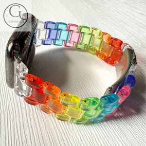 May include: A smartwatch with a link-style watch band made of translucent, multi-colored acrylic resin. The band features a repeating rainbow gradient of clear, red, orange, yellow, green, blue, and pink segments connected by metal pins.