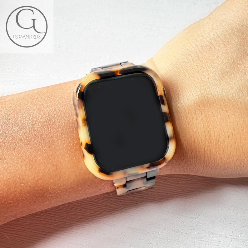 May include: A tortoiseshell patterned watch band with a black screen and a metal clasp.