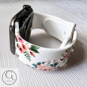 May include: White silicone Apple Watch band with a floral print featuring pink, red, and green flowers. The band is shown on a black Apple Watch.