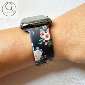 Puede incluir: Correa de reloj Apple negra con estampado floral de flores rosas, blancas y verdes. El reloj es negro. La marca "GOBANDZUS" está en la esquina superior izquierda.