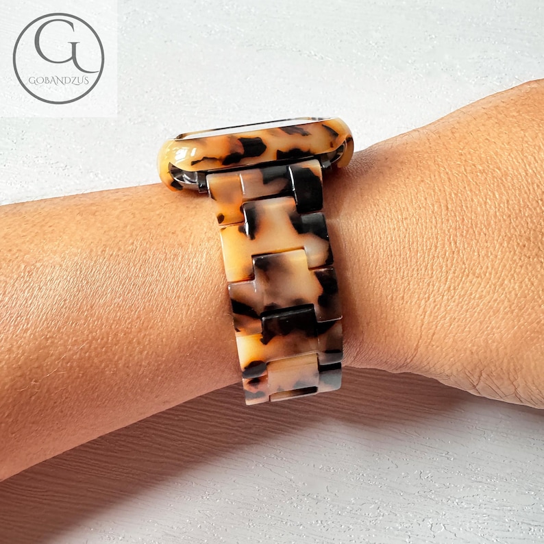 May include: A tortoiseshell patterned watch band with a black metal clasp. The band is made of a hard plastic material and has a glossy finish.