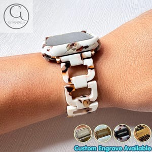 May include: A smartwatch band and protective case featuring a white, brown, and black tortoiseshell pattern. The band consists of interlocking rectangular links. Four small circular insets at the bottom display metal clasps with the text GOBANDZUS.