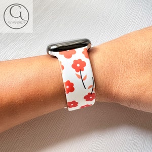 Puede incluir: Banda de reloj Apple blanca con un patrón floral rojo. La banda está hecha de silicona y tiene un diseño elegante.