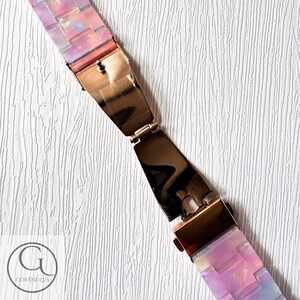 May include: A pink and purple iridescent watch strap with a rose gold clasp. The strap is made of a flexible material and has a unique, modern design.