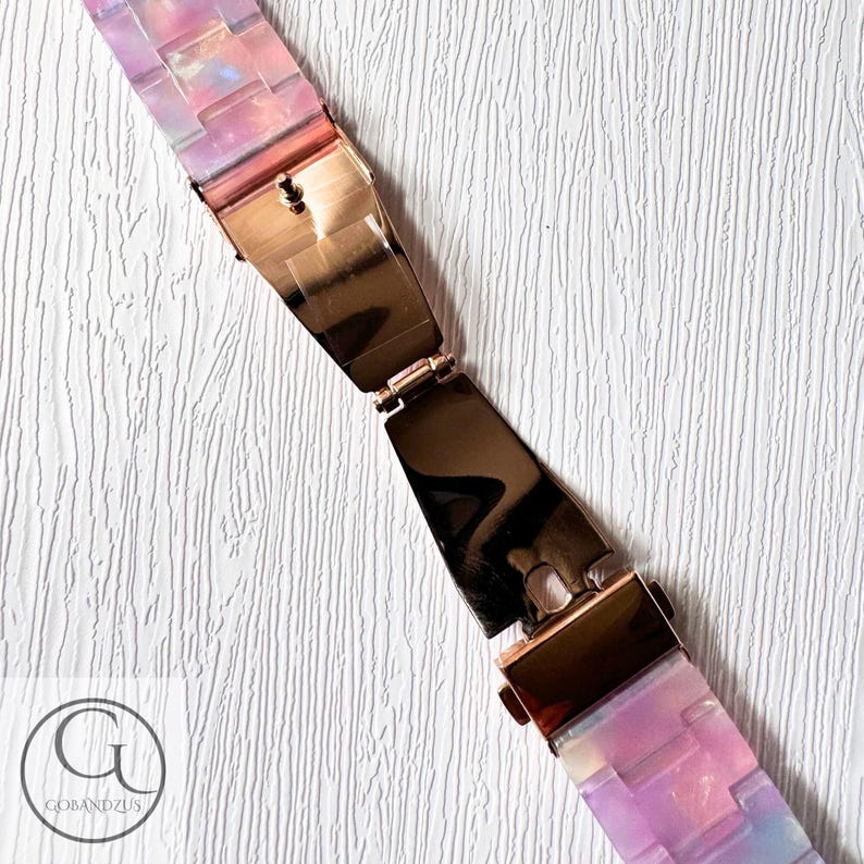 May include: A pink and purple iridescent watch strap with a rose gold clasp. The strap is made of a flexible material and has a unique, modern design.