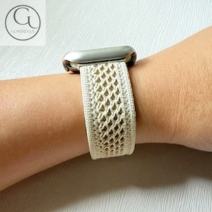 Puede incluir: Correa de Apple Watch color crema con un patrón de diamantes tejido. La correa está sujeta a una esfera de reloj plateada. La correa se lleva en la muñeca. El logotipo de la marca "GOBANDZUS" está en la esquina superior izquierda.