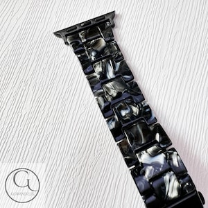 May include: Black and white marbled Apple Watch band with a black metal clasp.