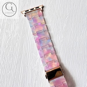 May include: A pink, blue and white patterned Apple Watch band with a rose gold metal connector.