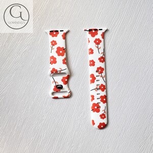 May include: White Apple Watch band with a red floral pattern. The band is made of silicone and has a buckle closure.