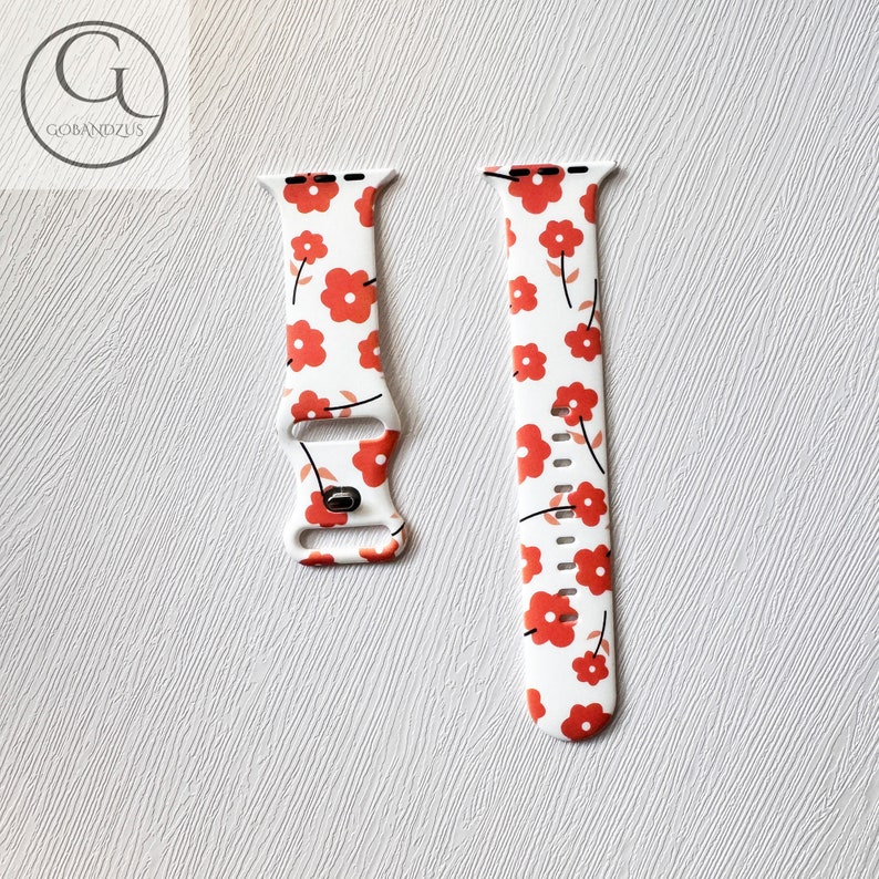 May include: White Apple Watch band with a red floral pattern. The band is made of silicone and has a buckle closure.