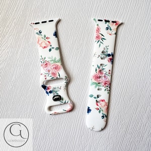 May include: White silicone Apple Watch band with a floral print featuring pink and blue flowers. The band has a white background with a floral pattern.