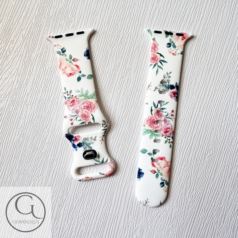 May include: White silicone Apple Watch band with a floral print featuring pink and blue flowers. The band has a white background with a floral pattern.