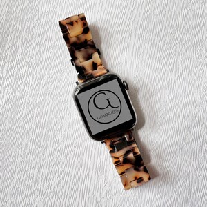 May include: A black Apple Watch with a brown and white tortoiseshell band. The watch face displays the logo "G" for "Gobandzus".