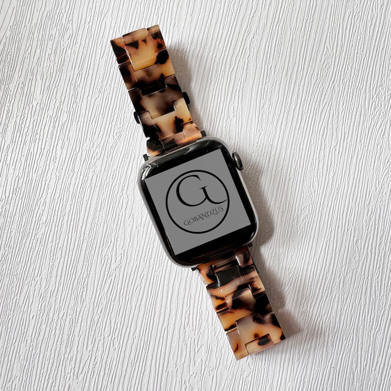 May include: A black Apple Watch with a brown and white tortoiseshell band. The watch face displays the logo "G" for "Gobandzus".